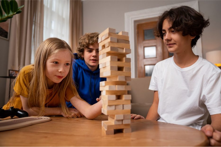 Три деца играят на настолна игра с дървена кула.
