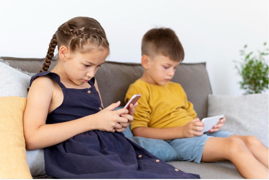 Две деца на диван с телефони в ръцете