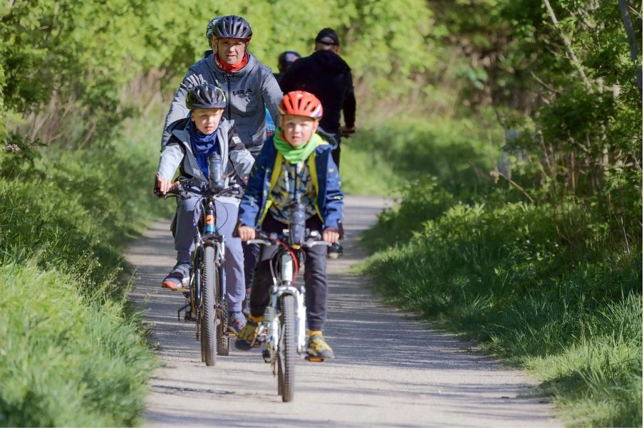 Деца, придружени от възрастни, карат велосипеди по планинска алея.