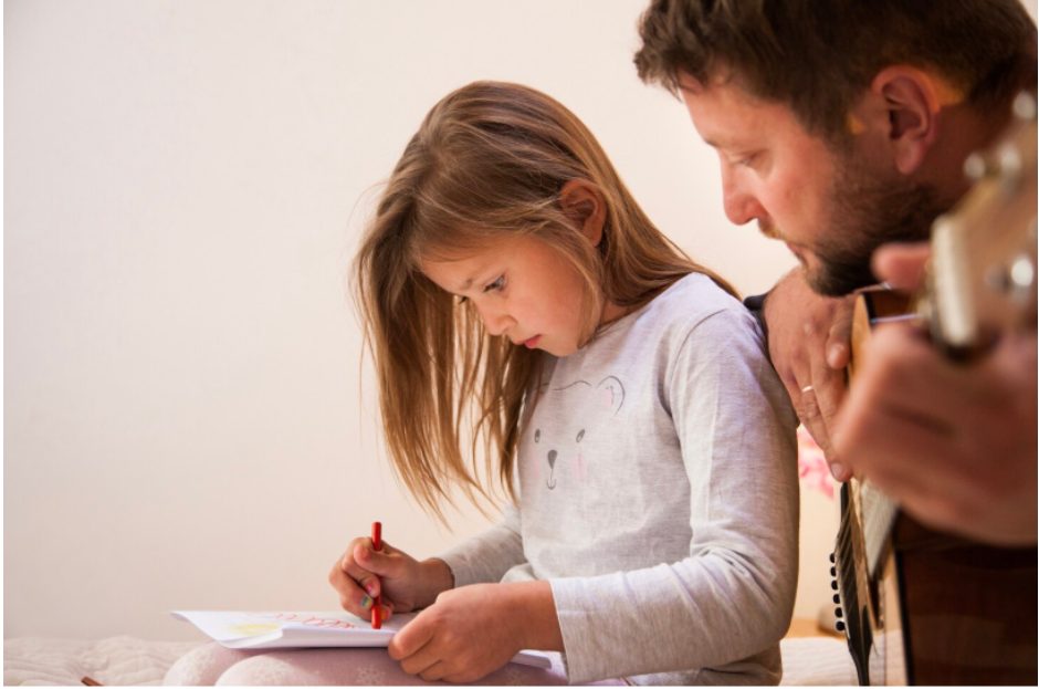 Дете рисува, докато родител свири на китара 