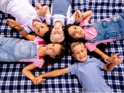 Деца лежат на одеало и държат ръцете си