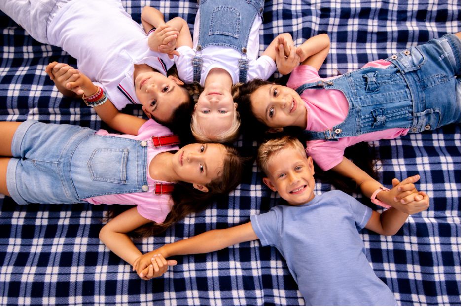 Деца лежат на одеало и държат ръцете си